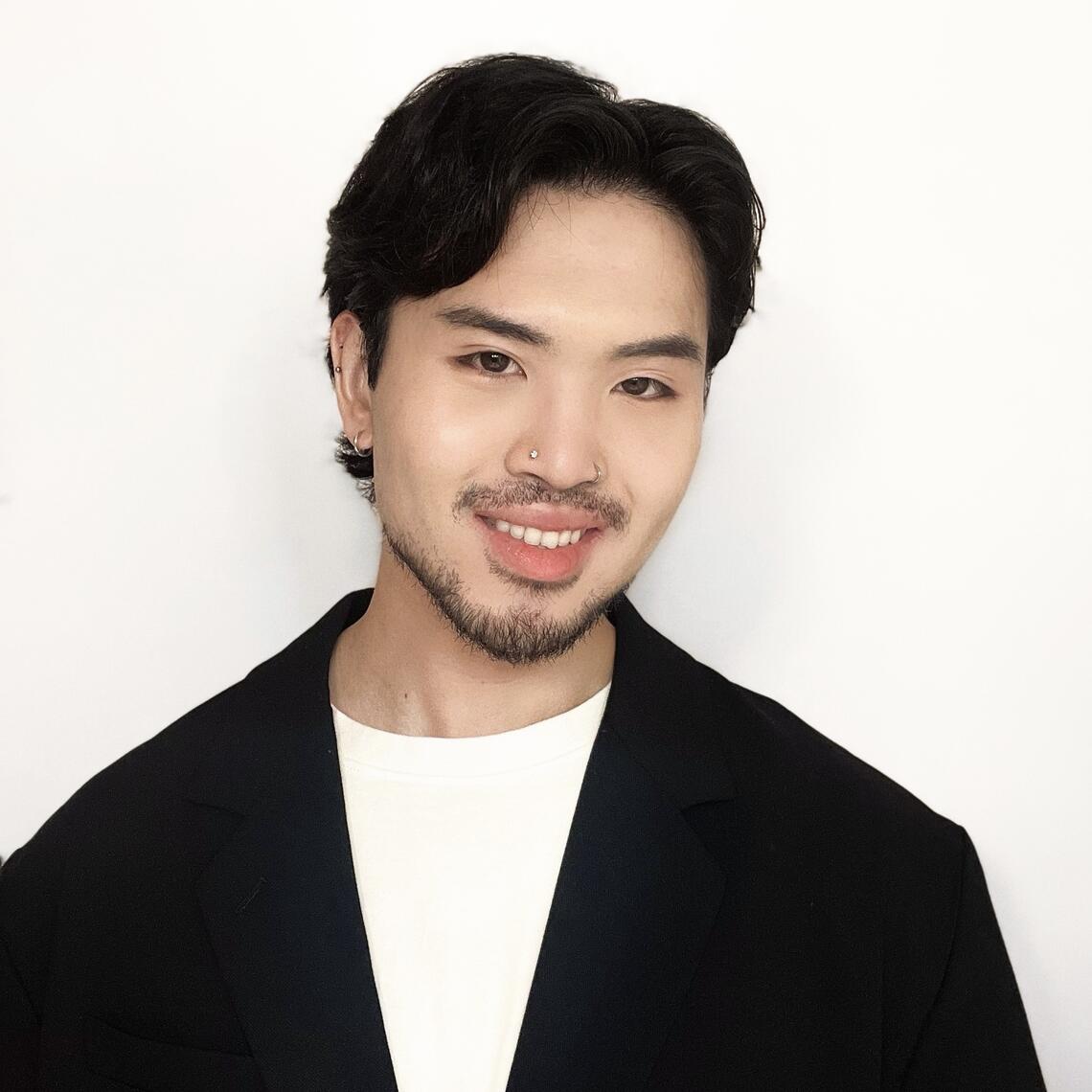 Eric Xie smiles in front of a white background wearing a black blazer and white t-shirt.